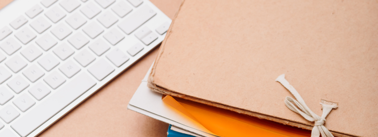 White keyboard on peach desk next to stack of notebooks tied with ribbon
