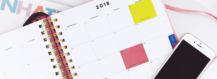 Open 2018 planner calendar with yellow and pink sticky notes and smartphone on desk