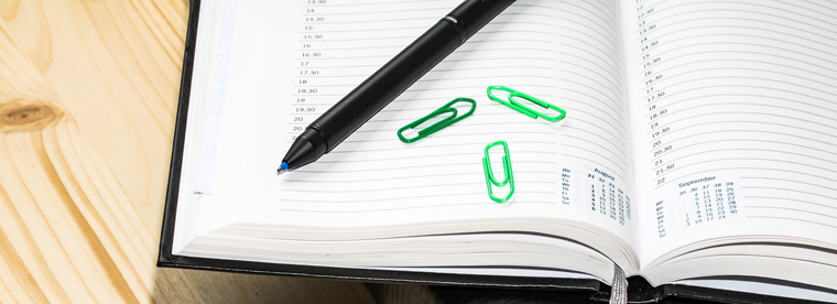Open daily planner with green paperclips and black pen on lined pages with calendar visible