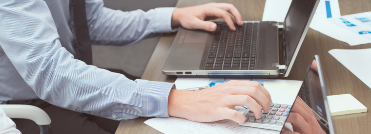 Person's hands on laptop keyboard and calculator at desk with business documents