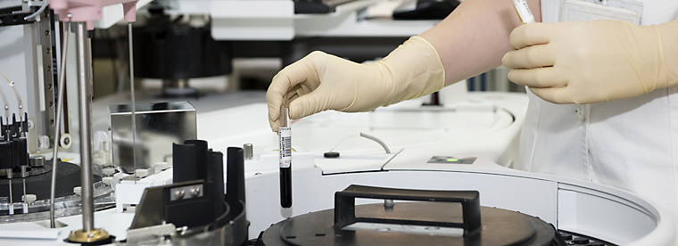 Laboratory technician in gloves handling blood sample near automated equipment