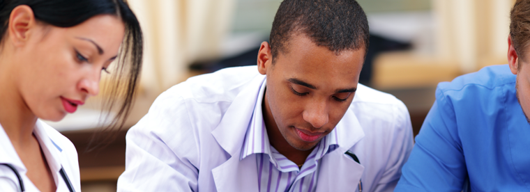 Young male professional in light purple shirt studying with colleagues in background